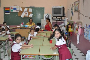 Young students in uniform seated in a classroom with teachers.