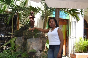 Woman in white tank top posing near a small statue and greenery.