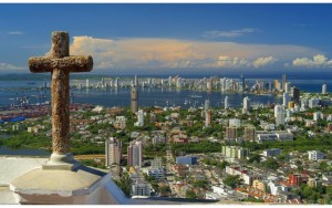 City view from a hilltop with a cross in the foreground under a clear sky.
