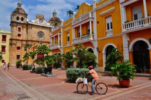 A child rides a bike in a vibrant, historic town square.