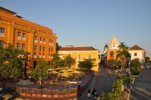 Sunny plaza with colorful buildings and outdoor seating under clear sky.