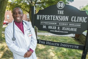 A smiling doctor stands beside a sign for The Hypertension Center.