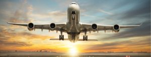 Airplane taking off at sunset with landing gear down.