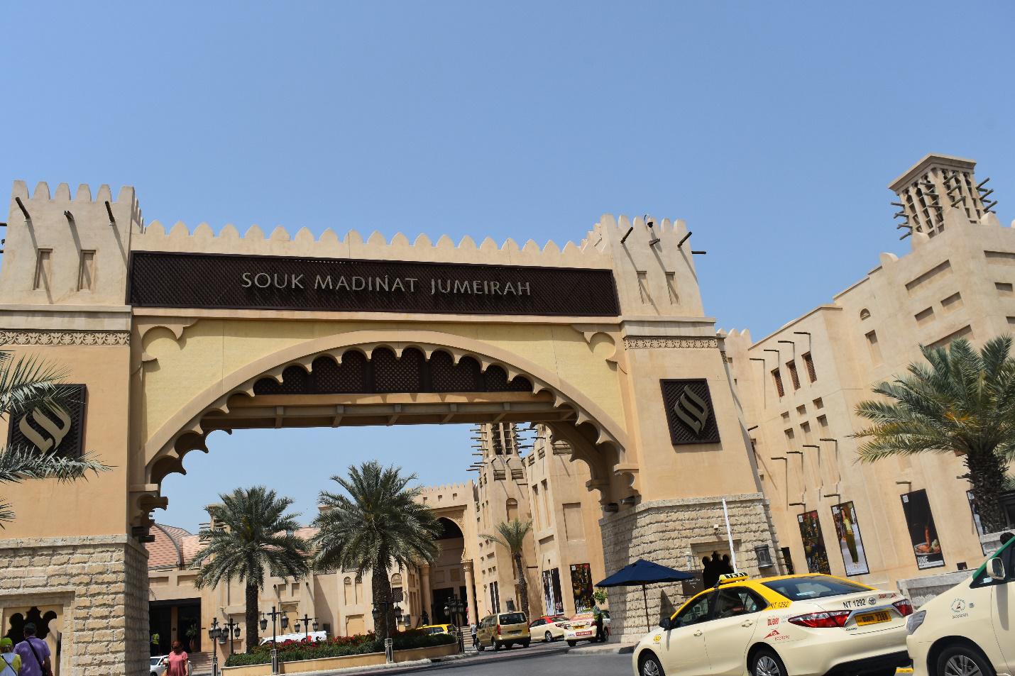 Entrance arch of Souk Madinat Jumeirah with taxis and palm trees nearby.